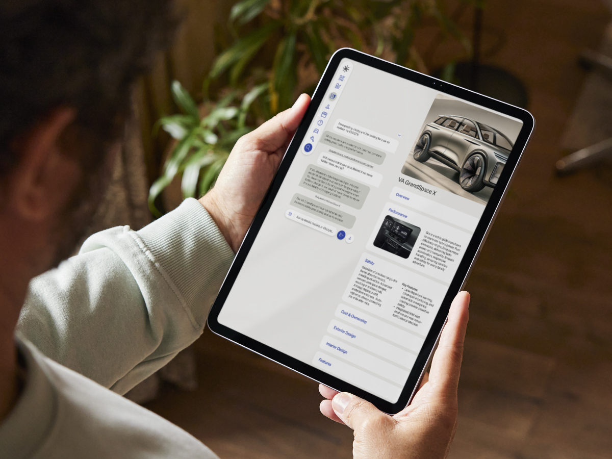 Person holding a tablet while browsing a car information app, displaying details and images of the VA GrandSpace X SUV.