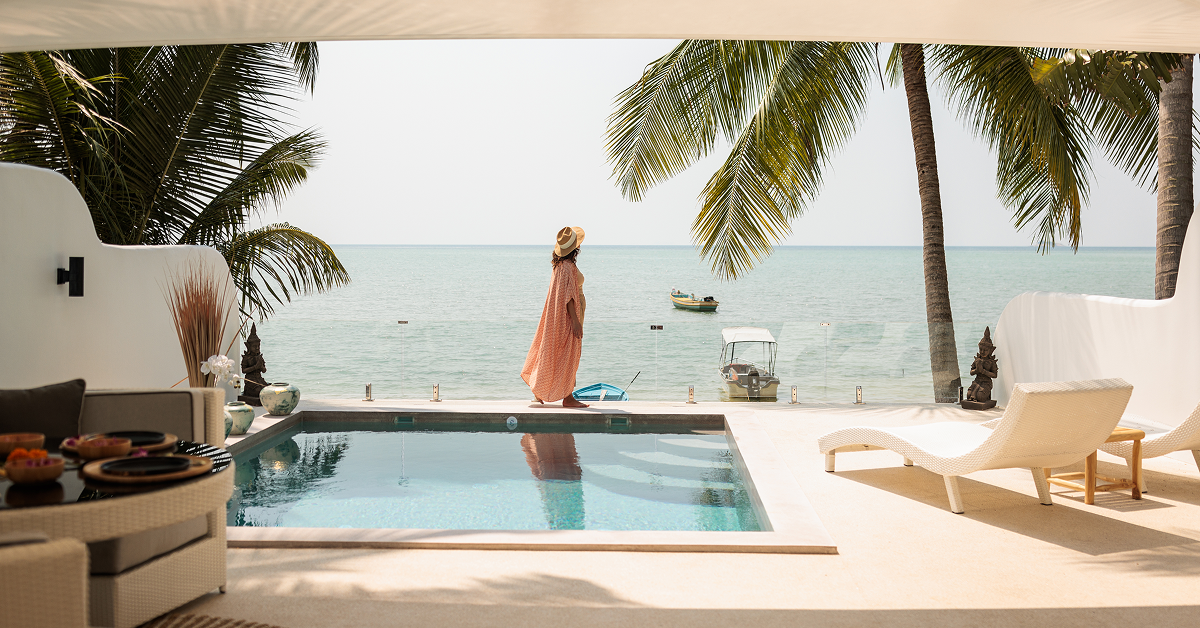 A sunny pool scene featuring a lounge chair and umbrella, with a beautiful beach in the background