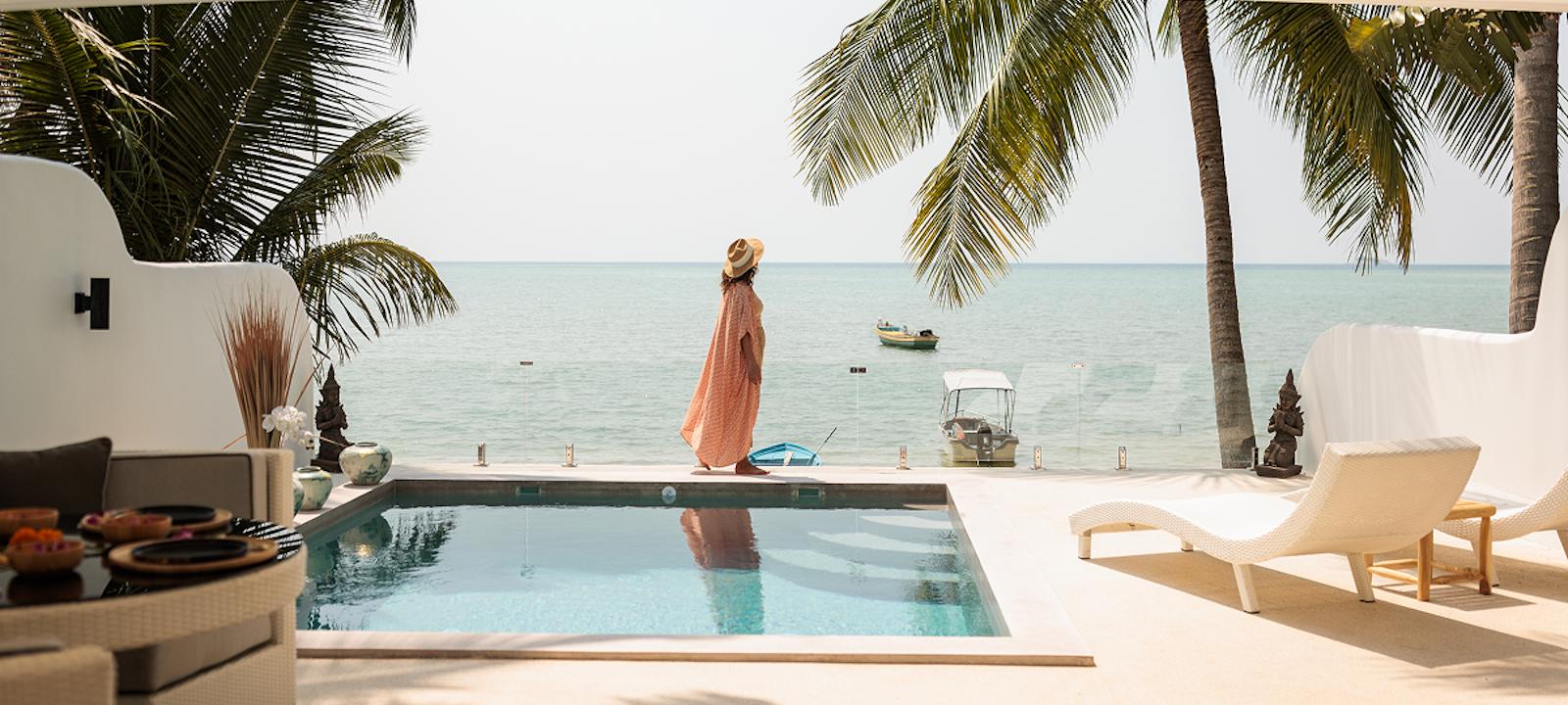 A sunny pool scene featuring a lounge chair and umbrella, with a beautiful beach in the background