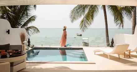A sunny pool scene featuring a lounge chair and umbrella, with a beautiful beach in the background