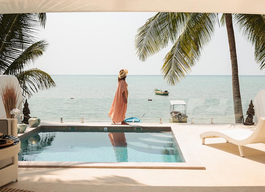 A sunny pool scene featuring a lounge chair and umbrella, with a beautiful beach in the background