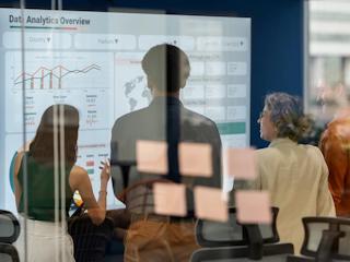 Business team reviewing a data analytics dashboard on a digital screen in a glass-walled office, emphasizing collaboration, insights, and performance metrics.