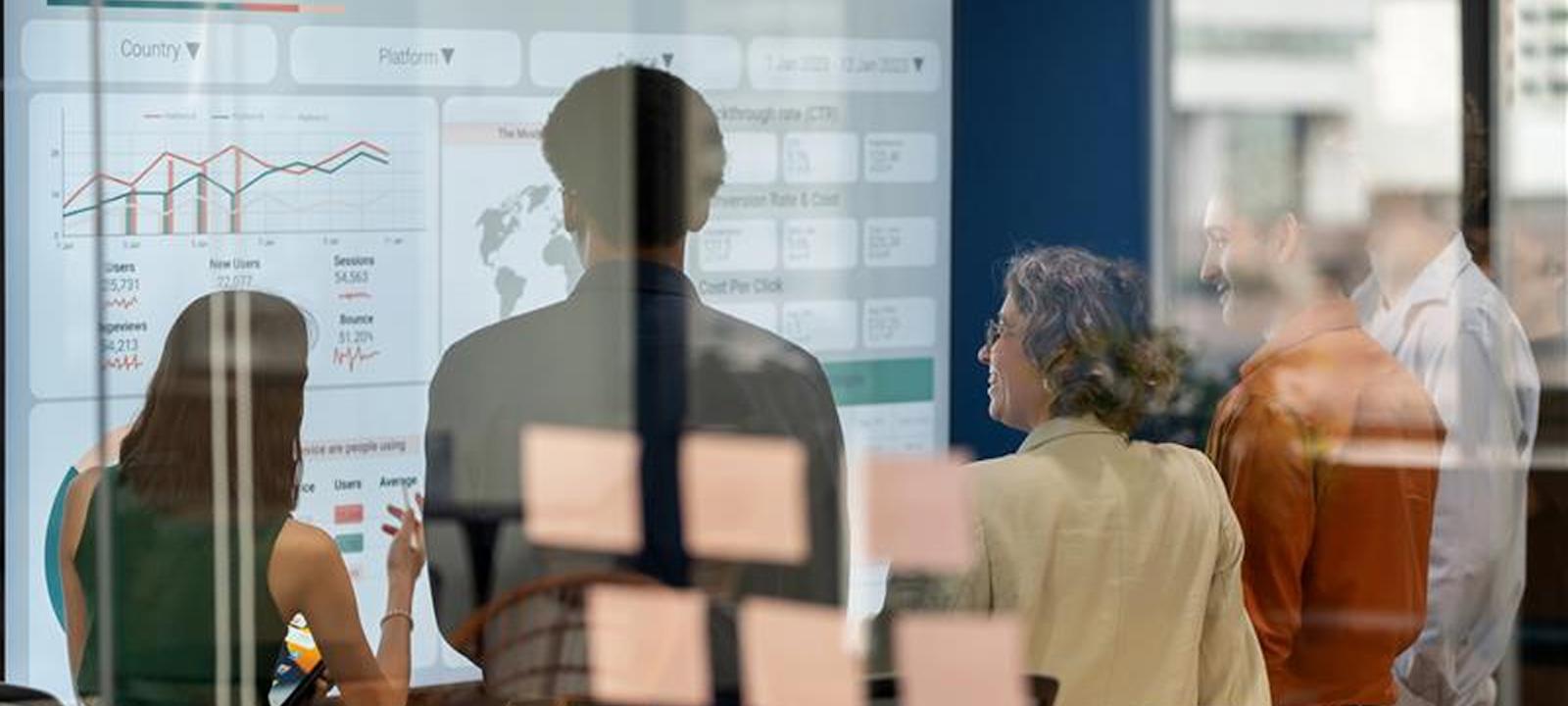 Business team reviewing a data analytics dashboard on a digital screen in a glass-walled office, emphasizing collaboration, insights, and performance metrics.