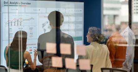 Business team reviewing a data analytics dashboard on a digital screen in a glass-walled office, emphasizing collaboration, insights, and performance metrics.