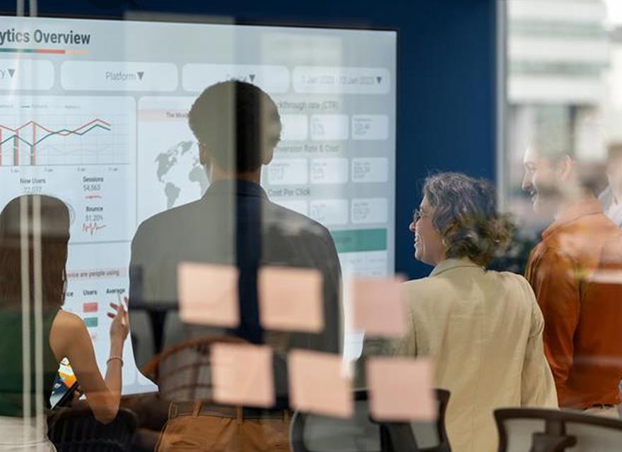 Business team reviewing a data analytics dashboard on a digital screen in a glass-walled office, emphasizing collaboration, insights, and performance metrics.