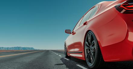 Close-up of a red sports car driving on an open highway under a clear blue sky, representing modern mobility and streamlined digital car experiences.