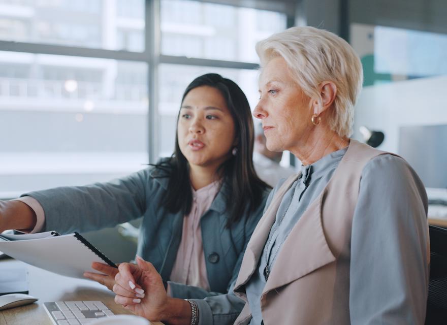 Two professional women reviewing data on a computer screen in a modern office, highlighting teamwork and digital business strategy.