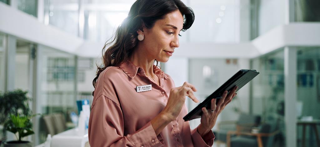 A woman in a pink shirt is focused on using a tablet, sitting comfortably in a well-lit room
