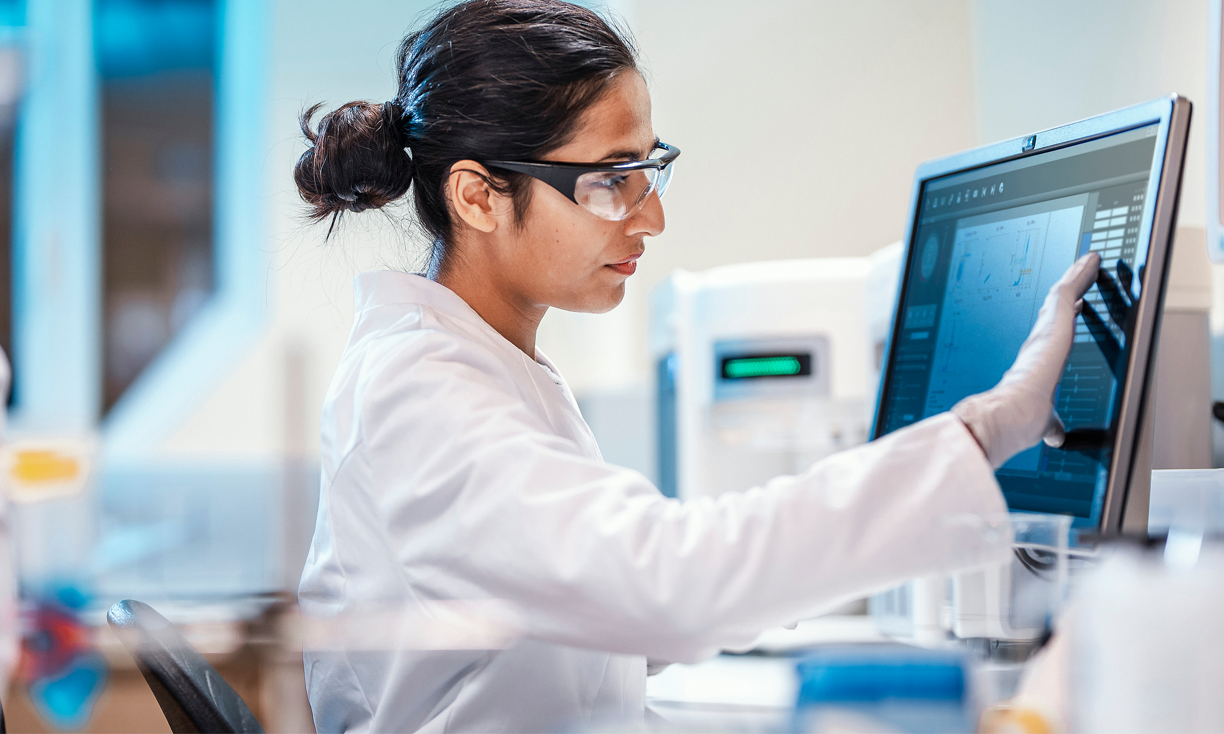 A woman in a lab coat is focused on her work at a computer in a laboratory setting