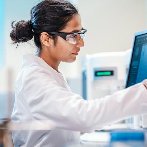 A woman in a lab coat is focused on her work at a computer in a laboratory setting