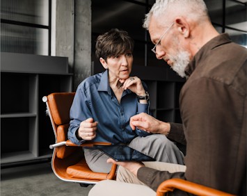 A man and a woman sit in an office, closely reviewing information on a tablet. The woman in a blue shirt listens intently as the man with gray hair explains something