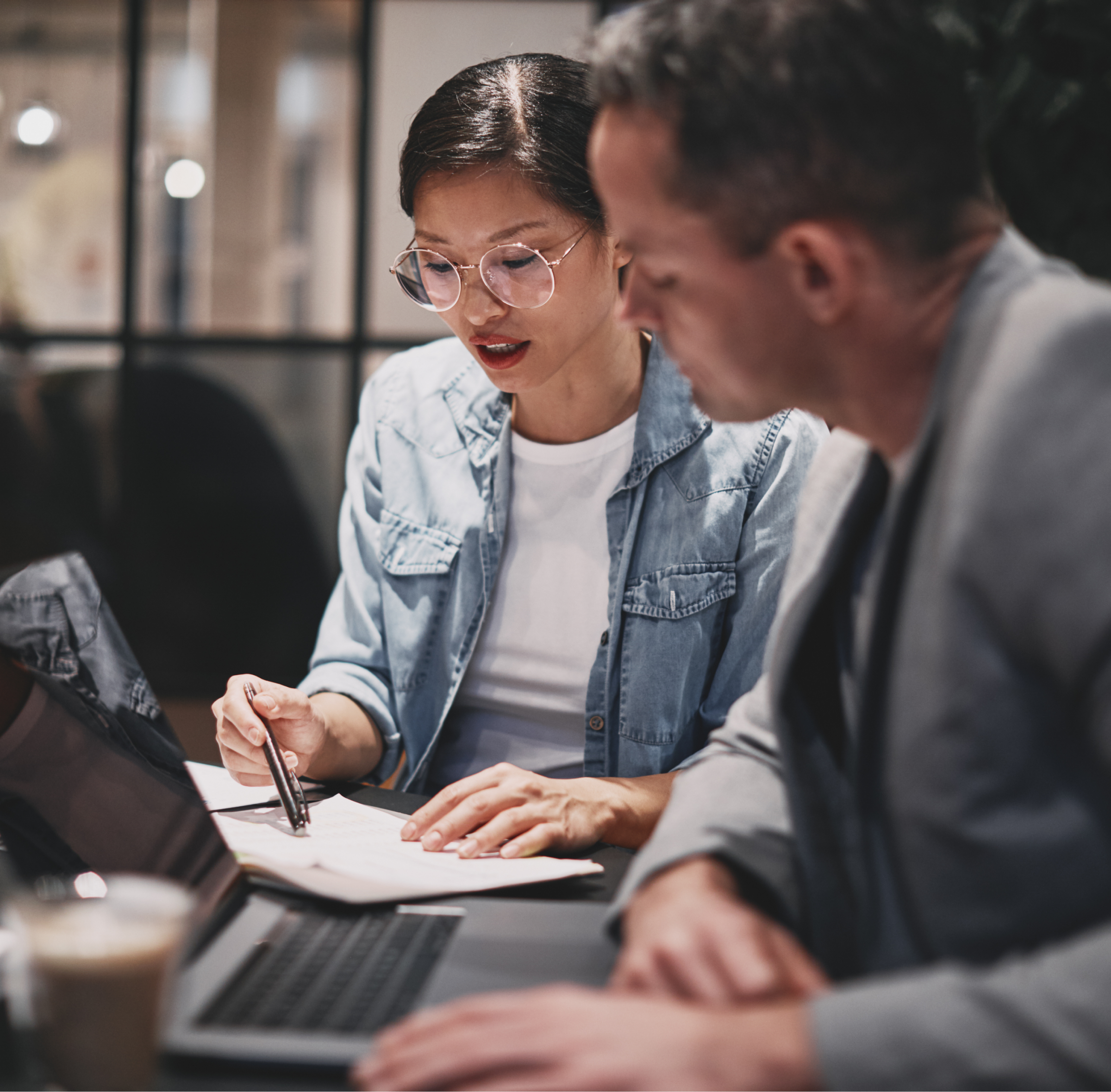 Two people actively collaborating over documents and a laptop in a modern workspace.