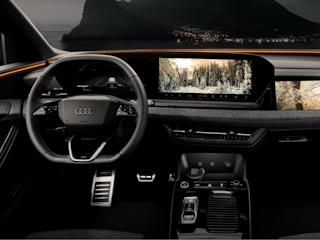 Interior view of a luxury Audi vehicle showcasing a sleek, high-tech dashboard. The digital display features multiple screens, including navigation with a snow-covered forest scene and a right-side monitor displaying a scenic image. Ambient lighting adds an orange glow, complementing the modern, minimalistic design. The background reveals a serene night landscape with a lake and mountains visible through the windshield.