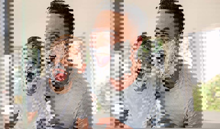 Caucasian father and son laugh at themselves in the mirror covered with shaving cream