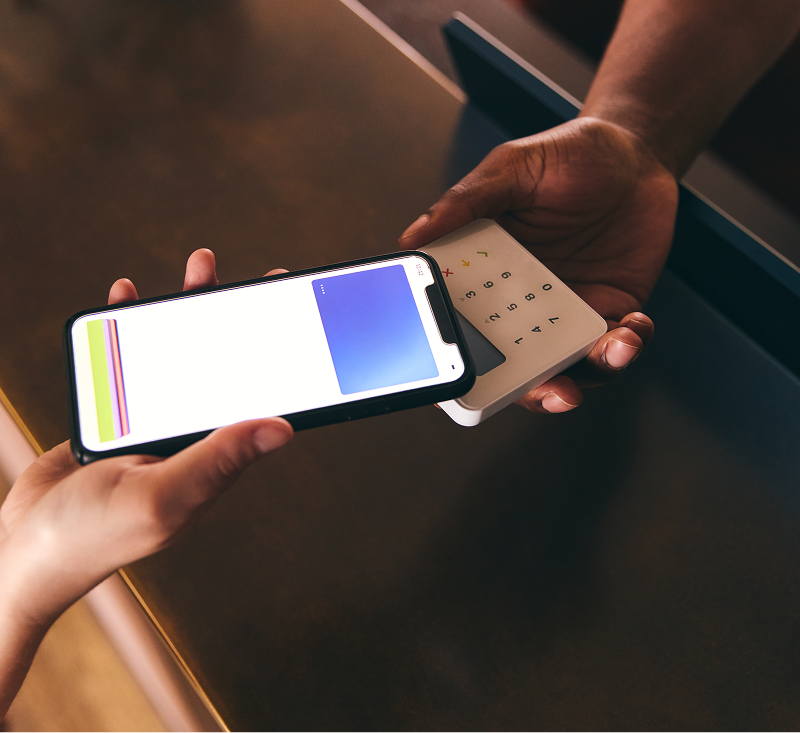 A person holds a smartphone in one hand and a credit card in the other, ready to make a payment