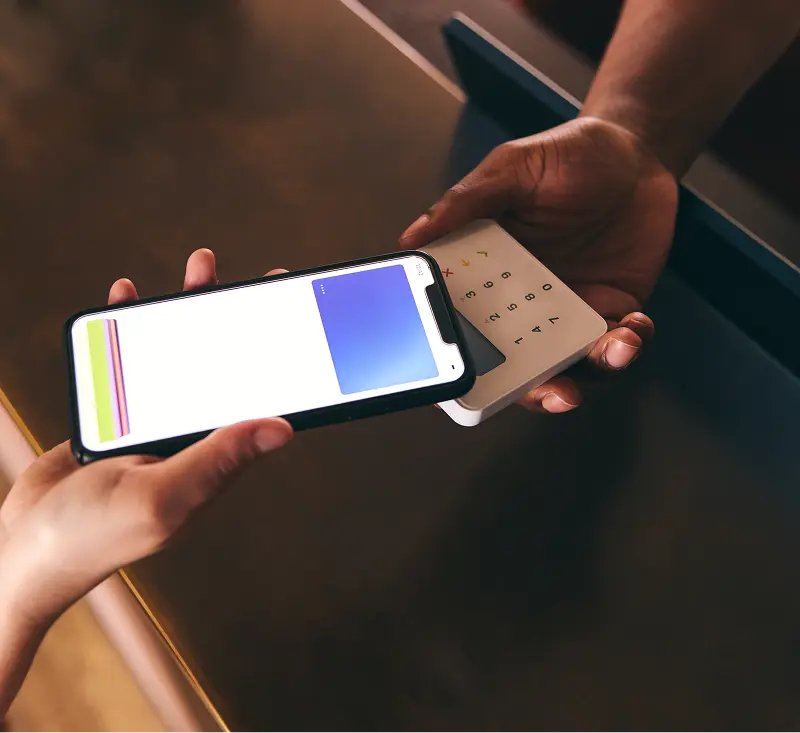 A person holds a smartphone in one hand and a credit card in the other, ready to make a payment