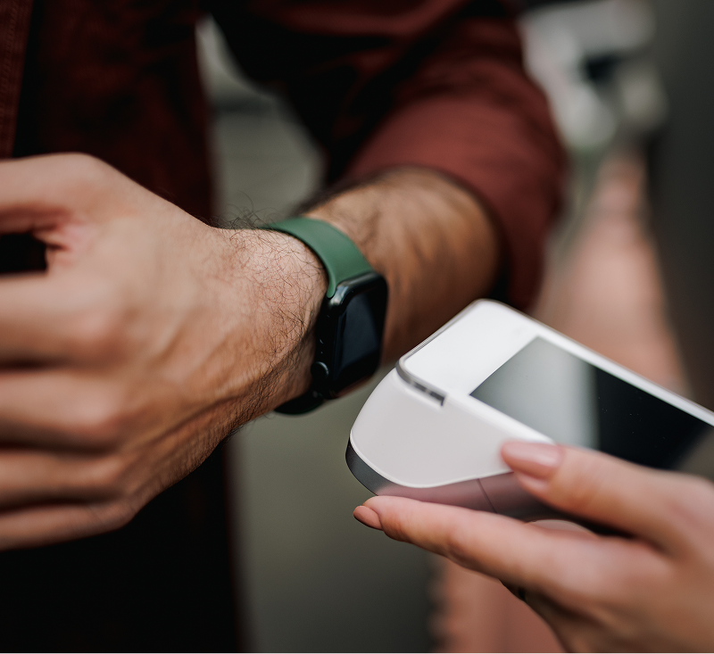 A person holds a watch in one hand and a credit card reader in the other, ready to make a payment