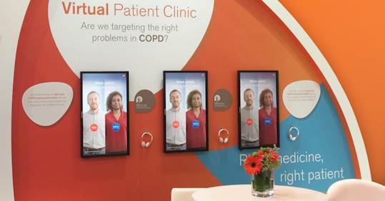 The image shows a display from a "Virtual Patient Clinic" focused on COPD (Chronic Obstructive Pulmonary Disease) with the question, "Are we targeting the right problems in COPD?" There are three digital screens featuring two patients, one labeled "Trevor" and the other "Eunice." Headphones are available below each screen for users to interact with or listen to content. The background includes bright colors and text that discusses personalized medicine and patient-focused care. A small round table with a flower vase is also visible in the foreground.