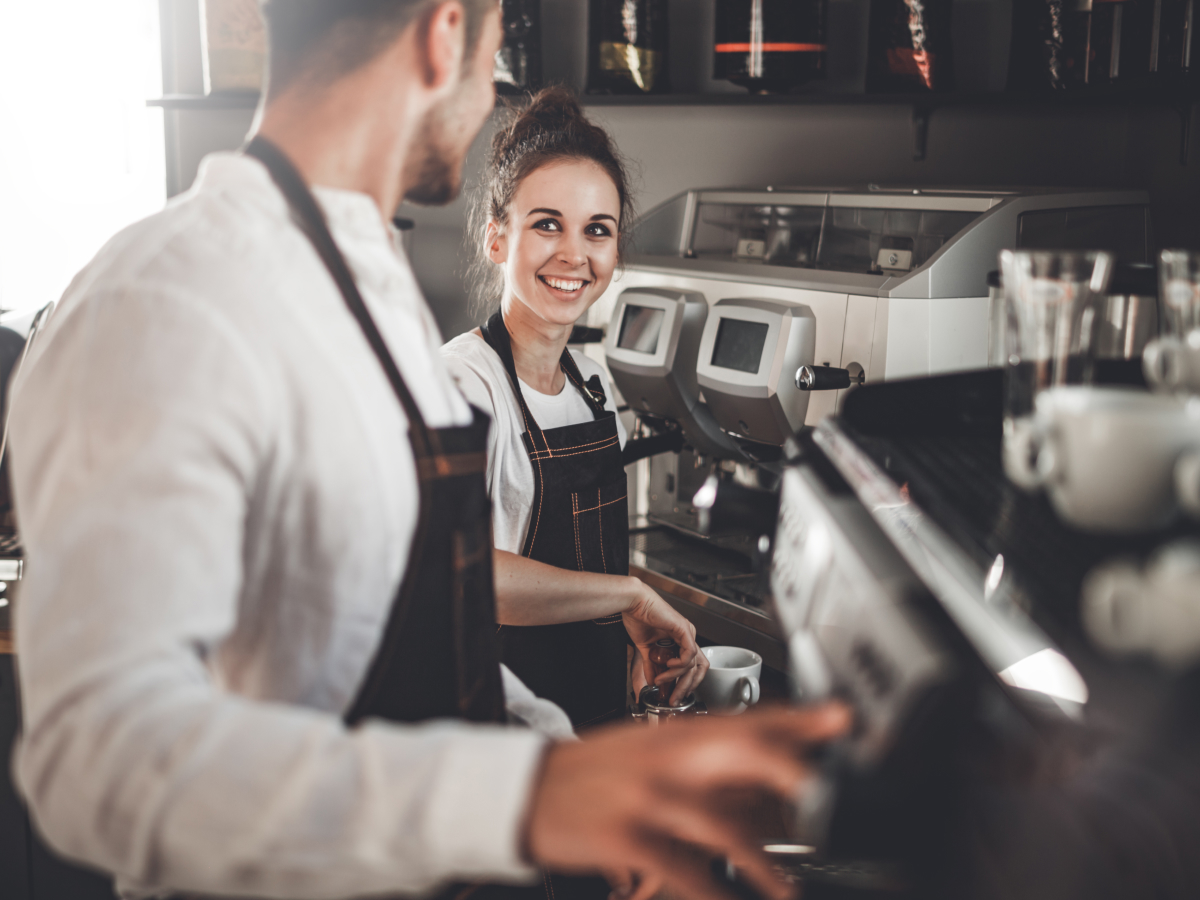 A cheerful man and woman collaborate in a coffee shop, showcasing teamwork and a friendly atmosphere.