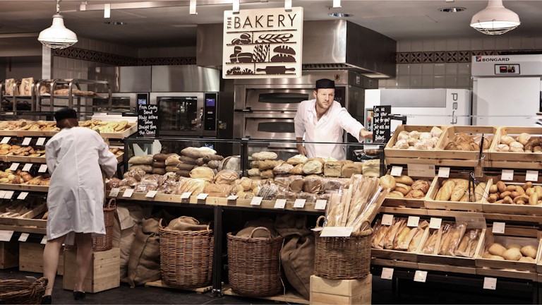 Two bakery workers are busy in a well-stocked bakery.