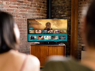 Two people sitting on a couch, watching a movie on a large television in a cozy living room setting.