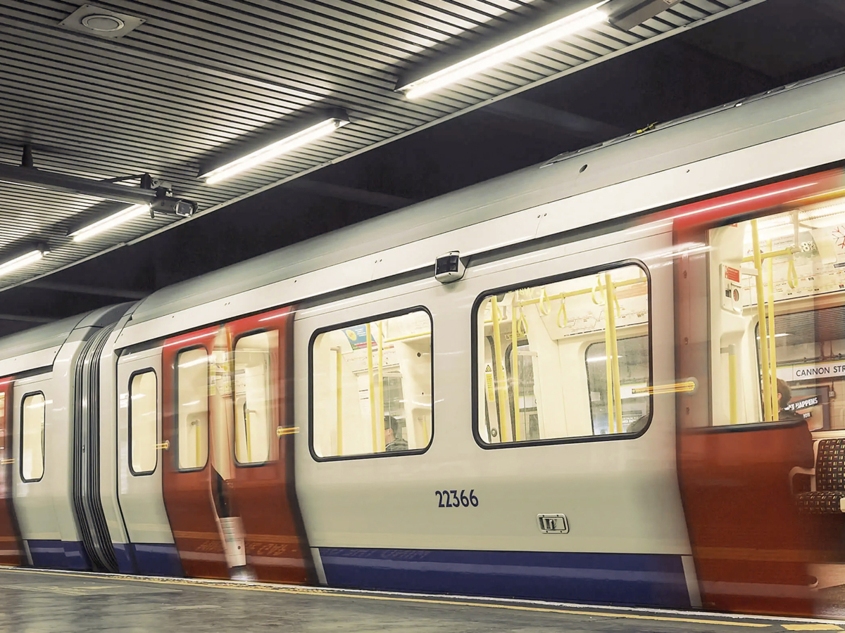 A London Underground train at Cannon Street station, captured in motion with blurred red and white doors. The train is illuminated under the station's bright lights, with empty seats visible through the windows.