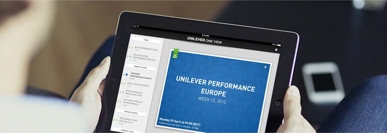 Two hands hold a tablet displaying a presentation slide titled "Unilever Performance Europe Week 12, 2013." In the top left of the presentation slide, there’s a green checkmark icon, possibly indicating the content is downloaded from the cloud. The screen also shows a side panel with a list of items, sorted by date, where each item has a green checkmark as well.