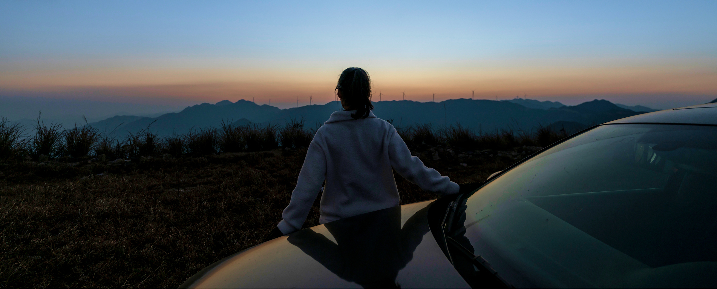 A woman stands beside a car, silhouetted against a vibrant sunset sky.