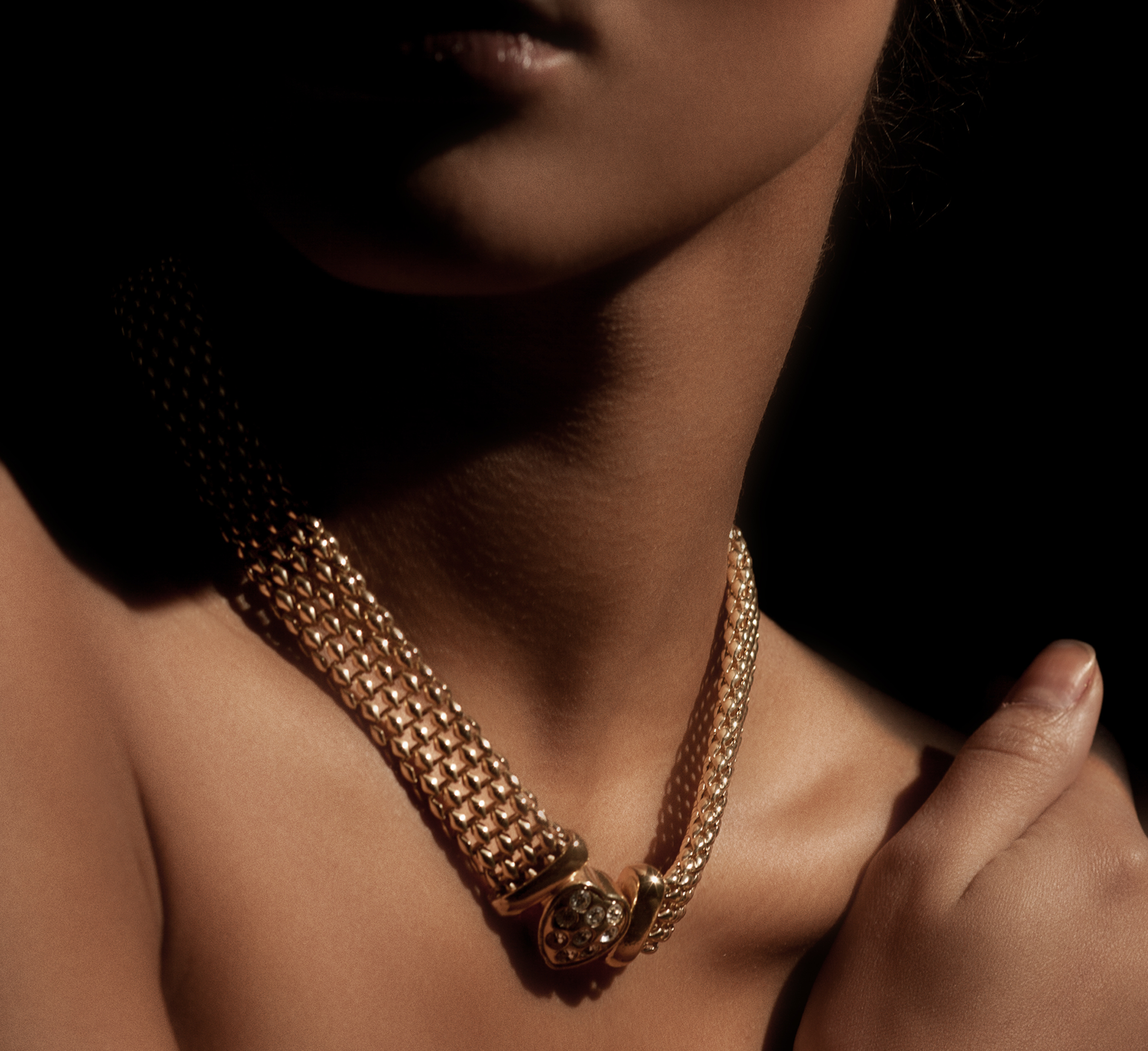 Close-up of a woman wearing an elegant gold necklace with intricate detailing, highlighting luxury jewelry in soft, dramatic lighting.
