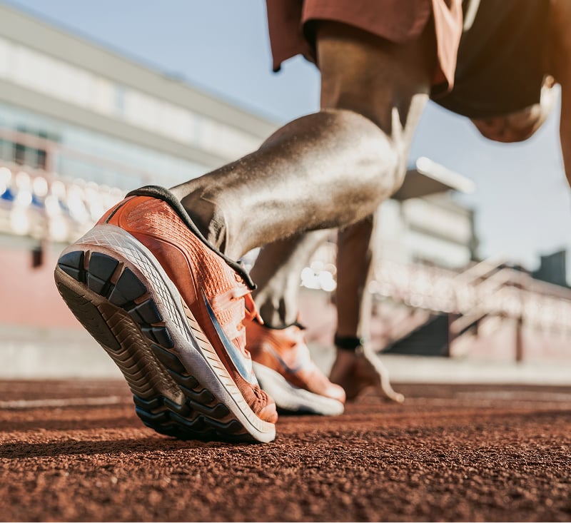 A man's legs positioned at the starting line of a running track, ready to begin a race.
