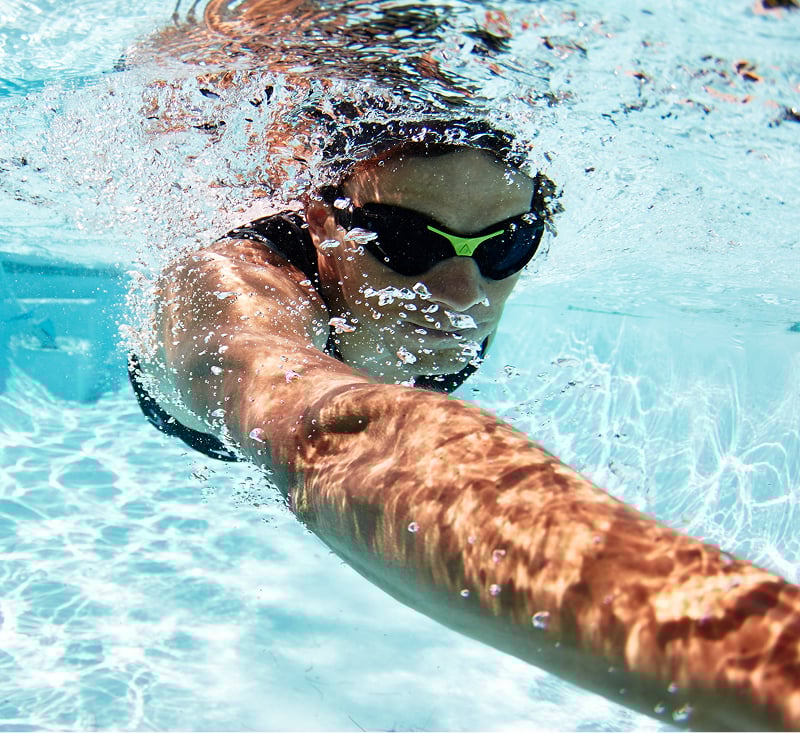 A woman swimming gracefully in a clear blue pool under bright sunlight.