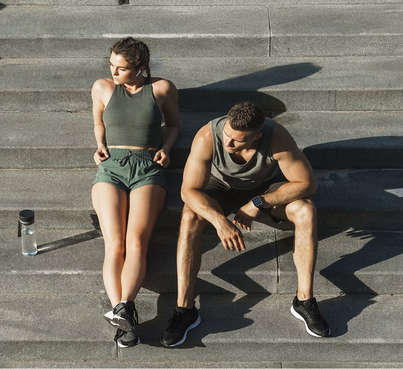 A man and woman sit on steps, each holding a water bottle, enjoying a moment of relaxation together.