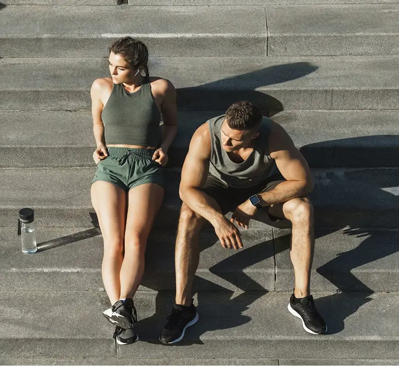 A man and woman sit on steps, each holding a water bottle, enjoying a moment of relaxation together.