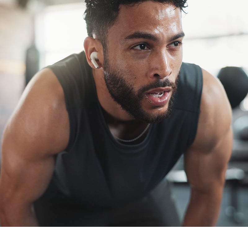 A man wearing earbuds is focused on his workout in a gym setting, demonstrating concentration and fitness.