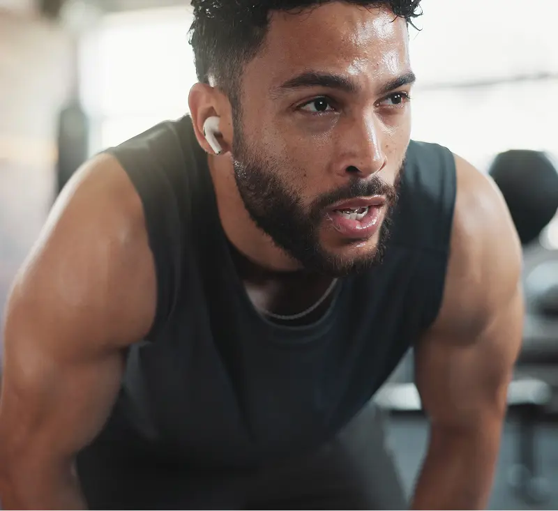 A man wearing earbuds is focused on his workout in a gym setting, demonstrating concentration and fitness.