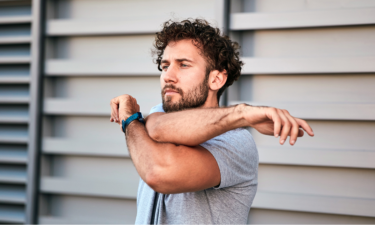 A bearded man stretches his arm upward, showcasing a moment of physical activity and flexibility.  