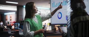 Female retail analyst presenting predictive analytics on a large digital screen, highlighting data-driven decision-making and immersive retail innovation.