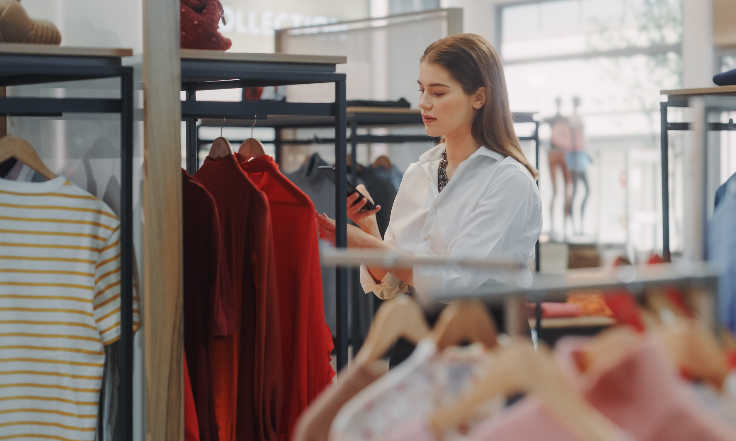 Retail associate scanning red clothing with a mobile device in a modern apparel store, highlighting inventory management and digital retail tools.