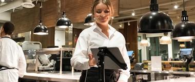 Restaurant staff member using a touchscreen POS system in a modern kitchen environment, showcasing agile retail and hospitality technology.