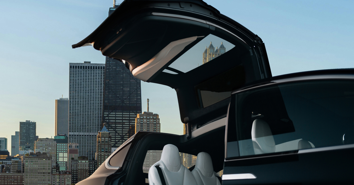 Luxury electric vehicle with open gullwing doors set against the Chicago skyline on a bright sunny day