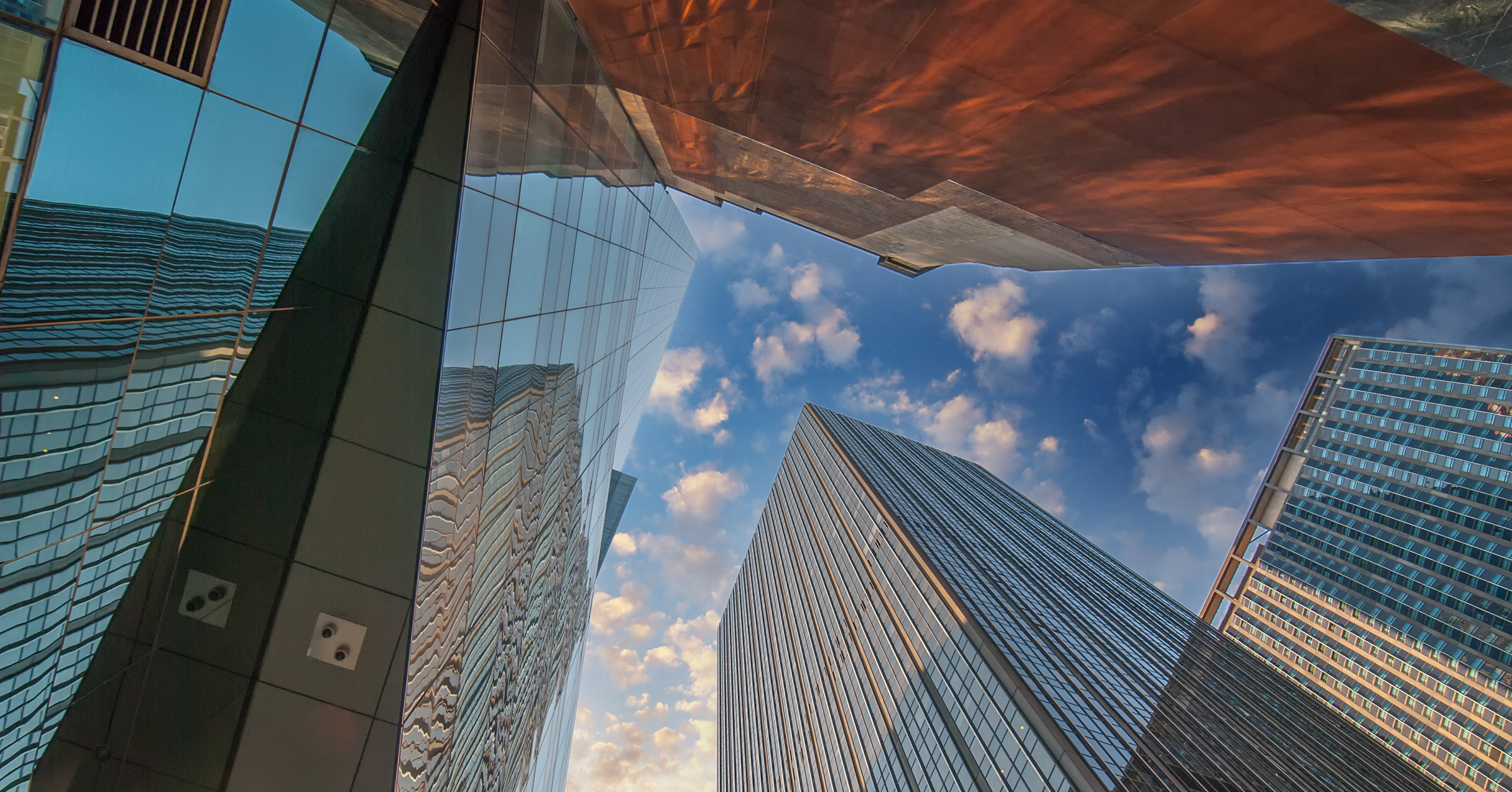 Upward view of modern glass skyscrapers reflecting a vibrant sunset sky, symbolizing innovation and the future of insurance