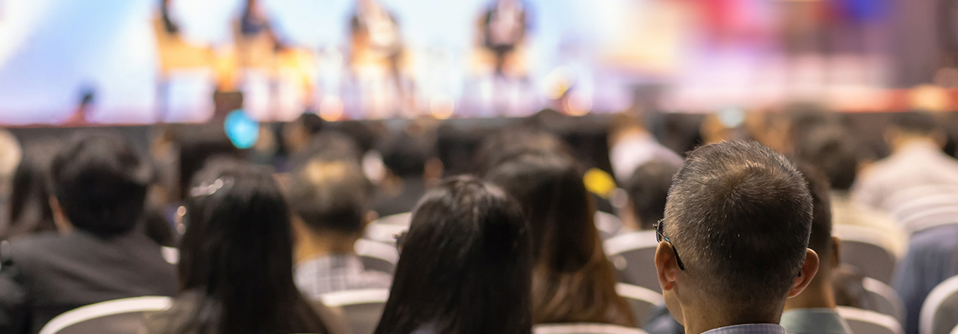 A large crowd of people seated in chairs, attentively listening at a conference event.