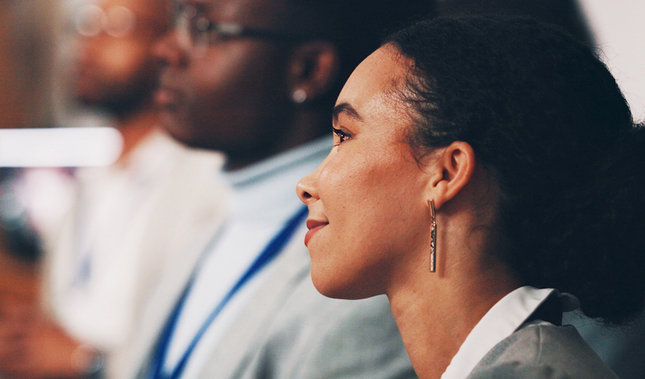 A woman sits among a group of people, looking engaged in the conversation around her.